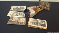 Wooden stereoscope viewer with several black and white stereoview cards laid out beside it, cards depict various architectural scenes.