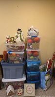 Stacked plastic bins with assorted Christmas ornaments, cookie jars shaped like snowman and house, gift bags, and other holiday items.