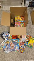 Open box with multiple comic books inside and several comics laid out in front. Visible titles include Archie, Betty and Veronica, Family Circus, and Garfield.