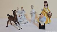 Photo showing all five vintage figurines arranged in a row including the Royal Ascot woman, Victorian couple, Beswick horse, Royal Doulton 'Fat Boy', and Lladro boy.