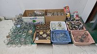 Overview photo showing large quantity of assorted mason jars and lids in boxes and bins on a tiled floor