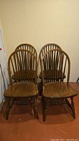 Four oak dining chairs grouped against a wall, front view