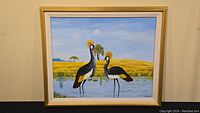 Full frontal image of painting framed 25.5x30 inches showing two crowned cranes standing in shallow water with yellow grass and sky background.