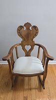 Front view of the rocking chair showing the carved backrest with shell motif and heart cutout, upholstered seat, and curved arms.