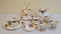 Full lot showing two-tier serving plate, teapot, 2 teacups and saucers, nut dish, and 3 coffee mugs with rose floral pattern and gold accents.