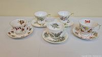 Wide shot showing all five Royal Albert tea cups with matching saucers arranged in a single line.