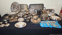 Photo of entire silver and silverplate collection including trays, bowls, candelabras, flatware, and serving dishes on a table.