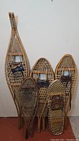 Six snowshoes of varying sizes propped against a wall, showing full lot and size range