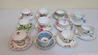 Top view showing 10 assorted vintage tea cups and saucers with floral and gold detailing arranged in a clustered layout.