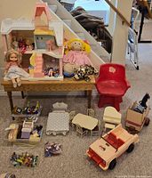 Full lot overview showing dollhouse on table with dolls, horse trailer, jeep, furniture, and red chair in front.