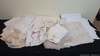 Lot of folded table linens including plain white and cream fabrics, crochet lace trims and embroidered pieces.
