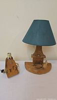 Full view of the lamp with blue fabric lampshade and wooden carved base with lady and fireplace