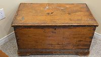 Front view of a vintage wooden trunk with visible surface wear, scratches, and paint marks.