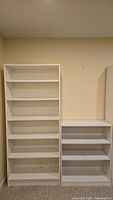 Two white shelving units side by side against a beige wall, one taller with six shelves and one shorter with three shelves.