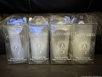 Front view of four unopened Jazzy Candle flameless tea lights in clear plastic boxes, showing product label and flame icon.
