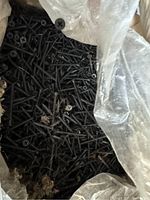 Opened box with visible black drywall screws inside a plastic bag lining, screws mostly uniform size and condition, showing some dirt and debris inside box.