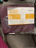 Photo of the full length hanging coat organizer in its original plastic packaging. The label visible on the packaging reads the dimensions and features including separate boot/shoe pockets and full organizer length.