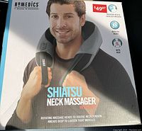 Front of box showing image of neck massager around a model's neck, brand Homedics, highlights of features such as kneading neck and shoulder massage, rotating heads, and heat function.