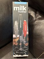 Front view of the retail box showing three milk frothers in black, red, and grey colors with stands.