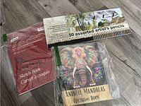 Photo showing a tin of 50 assorted artist's pencils, a 30-page sketch book, and an Animal Mandalas adult coloring book with an elephant design on cover.