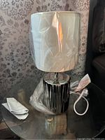 Photo of the petite table lamp showing the chrome base and white fabric shade wrapped in protective plastic.