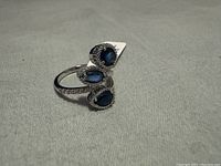 Ring displayed lying on its side showing three blue sapphire stones and milgrain detailing.