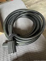 Coiled black pressure washer hose on grey fabric surface.