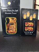 Box packaging showing branding and images of the solar mason jar light with glowing LED lights inside the jar.