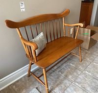 Front view of a country style wooden bench with a decorative cushion on tiled flooring.