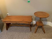Wooden bench and round top side table placed on carpet against wall, showing full side view of bench and side table