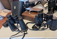 Photo shows three different binoculars together and their respective cases/pouch on a table.