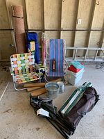 Wide view showing two vintage lawn chairs, cooler, bucket, emergency light, two folded camping chairs in bags, and rolled rug