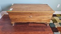 Front view of the wooden cedar chest showing carved medallion detail and wear on top.