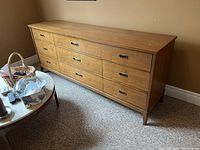 Front angle view of nine drawer wooden dresser showing metal hardware and wear on wood surface.