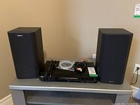 DVD player and two speakers on a shelf with cables coiled on top of DVD player.