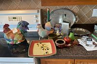 Overall view of Fitz and Floyd rooster cookie jar and assorted kitchenware on counter including ceramic plate, wood chicken figure, metal trays, grater and small decorative items