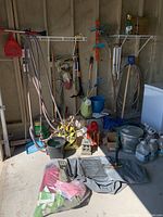 Wide view of a variety of gardening tools including shovel, rake, hoses, watering jugs, Kenmore vacuum, and garden ornaments.