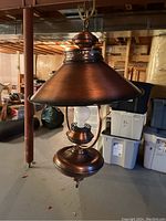 Full view of the hanging metal light fixture showing bronze/copper finish, conical metal shade, and exposed bulb socket.