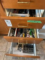 Three open kitchen drawers showing cutlery and kitchen utensils including knives, scissors, whisks, graters, and wooden spoons.