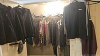 View of multiple clothing items hanging on racks showing coats, shirts, pants, Adidas sweater, some hats and boots on floor