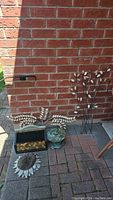 Outdoor arrangement of metal leaf wall art, metal box, birdcage, and metal sun decoration on brick patio