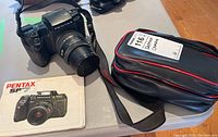 Photo showing Pentax SF7 camera with Pentax-F zoom lens attached, carry pouch and manual on table.