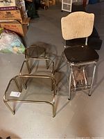 View of three metal framed side tables of varying sizes and vintage aluminum framed kitchen stool with vinyl seat and backrest, situated on concrete floor.