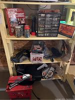 Three shelves filled with various corded power tools, hardware in jars and small drawers, books including Ortho's Home Improvement Encyclopedia, and a shoeshine kit on yellow metal shelves.