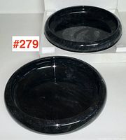 Two round black marble bowls shown, one resting on white packing material, black with gray and white veining, polished surface.