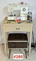 Wide view of Singer sewing machine atop a small table with a wooden sewing cabinet underneath and various accessories on the table.