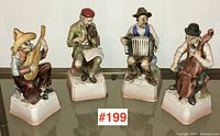 Four Japanese bisque porcelain music box figurines shown together on a reflective surface. Each depicts a seated musician playing a different instrument.