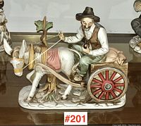 Front view of the bisque porcelain figure of a man smoking a pipe on a donkey cart with detailed red wheels and sacks in the cart.