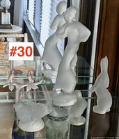Wide view of five Bohemian satin finish crystal figurines placed on glass shelves including a woman, bird, rabbit, and small birds on branch.