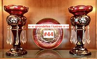 Two ruby red Bohemian glass girondelles with crystal prisms displayed side by side in a wooden cabinet.